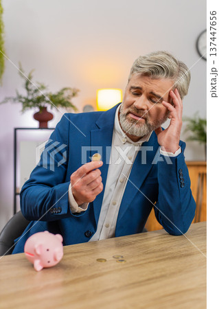 Middle-aged businessman shakes piggy bank counts coins worried about debt bankruptcy planning budget 137447656