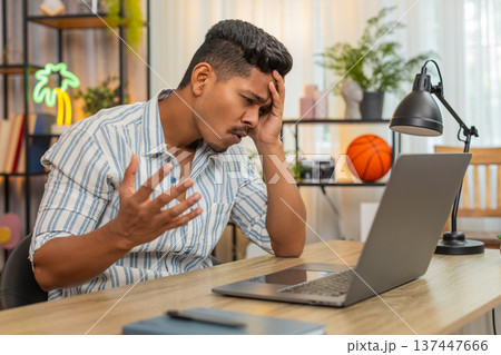 Indian man reads bad project news on laptop sighs feels defeat loss failure after overdue deadline 137447666
