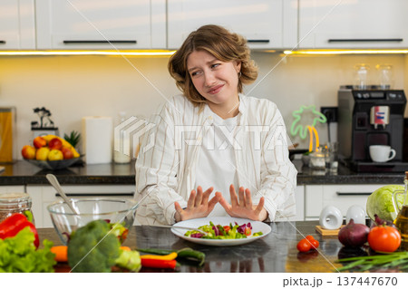 Young woman refusing healthy salad during weight loss diet struggle with upset mood in home kitchen 137447670