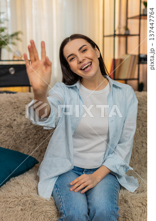Young woman sitting on sofa smiling cheerfully waving hand hello greeting friendly welcoming gesture Young woman sitting on sofa smiling cheerfully waving hand hello greeting friendly welcoming gesture 137447764