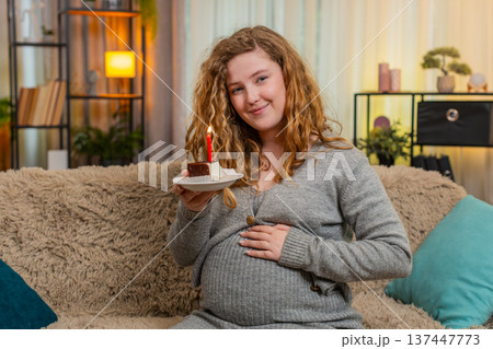 Pregnant woman making birthday wish blowing out cake candle celebrating special home moment 137447773