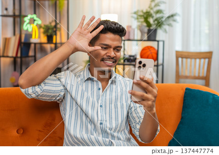 Indian man on video chat with friend laughs waves hello goodbye shows ok sign during chat smiles fun 137447774