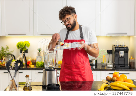 Arabian young adult man adding apple and banana to blender for smoothie breakfast in house kitchen 137447779