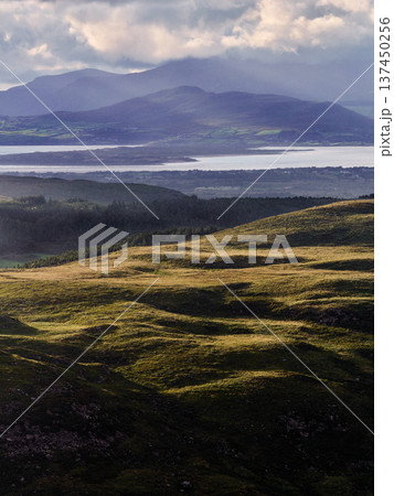 Hillsides glow under the soft light. Mountains stand silhouetted in the distance. Hillsides glow under the soft light. Mountains stand silhouetted in the distance. 137450256