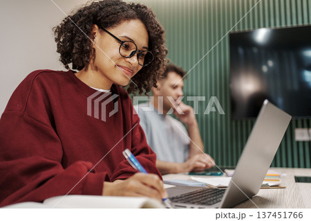 Woman Studying With Pen And Glasses. Young Lady Engaged In Study With Laptop And Attentive Expression 137451766