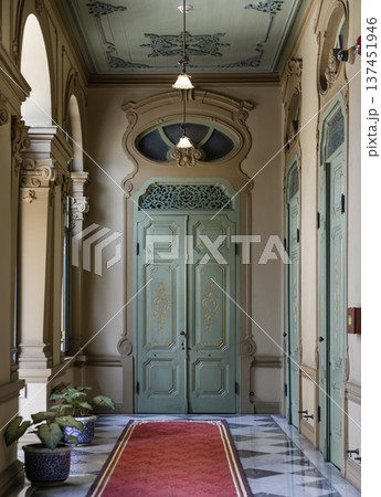 An ornate hallway in Bang Khun Phrom Palace featuring European-influenced architectural details. The design centers on a pale mint green double door with intricate carvings and an oval transom. An ornate hallway in Bang Khun Phrom Palace featuring European-influenced architectural details. The design centers on a pale mint green double door with intricate carvings and an oval transom. 137451946