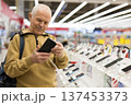 elderly man examines tablet computer in showroom of electronics store 137453373