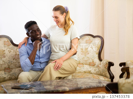 Happy couple in love embracing while sitting on vintage sofa indoors Happy couple in love embracing while sitting on vintage sofa indoors 137453378