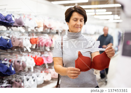 Older woman picking out bra in clothes department of supermarket Older woman picking out bra in clothes department of supermarket 137453381