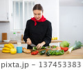 Smiling female chef in black uniform preparing vegetable salad in private kitchen 137453383