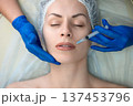 Female head in medical cap lying on a couch and get professional cosmetic injection in nasolabial fold area, aesthetic medicine procedure with doctor hands in blue gloves, close-up 137453796