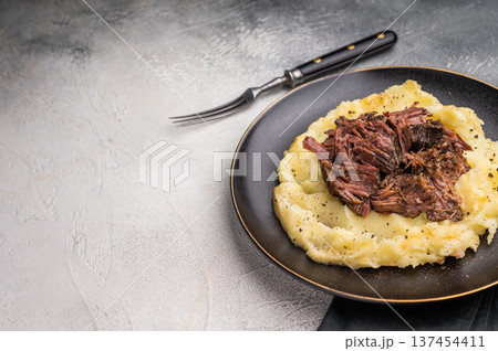 German Braised Beef Cheek, Slow cooked meat with smashed potatoes on a plate. grey background. top view German Braised Beef Cheek, Slow cooked meat with smashed potatoes on a plate. grey background. top view 137454411