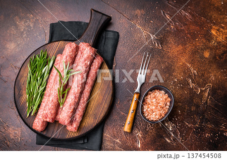 Fresh raw beef and lamb meat kebabs sausages on wooden board. brown background. top view Fresh raw beef and lamb meat kebabs sausages on wooden board. brown background. top view 137454508