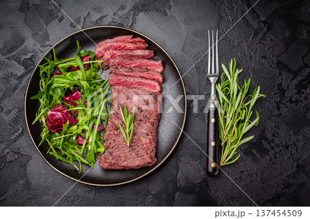 Grilled and sliced Flank beef steak on plate with salad. black background. top view Grilled and sliced Flank beef steak on plate with salad. black background. top view 137454509