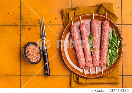 Raw Turkish Urfa kebab skewers on a plate with herbs. orange background. top view Raw Turkish Urfa kebab skewers on a plate with herbs. orange background. top view 137454529
