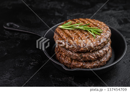 Grilled beef and lamb hamburger patty with seared crust and juicy texture in cast iron skillet. Cooked mixed meat on dark stone background. Grilled beef and lamb hamburger patty with seared crust and juicy texture in cast iron skillet. Cooked mixed meat on dark stone background. 137454709