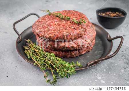Raw Uncooked beef lamb minced meat patty with herbs and pepper in pan. Overhead view on light stone background with copy space. Raw Uncooked beef lamb minced meat patty with herbs and pepper in pan. Overhead view on light stone background with copy space. 137454718