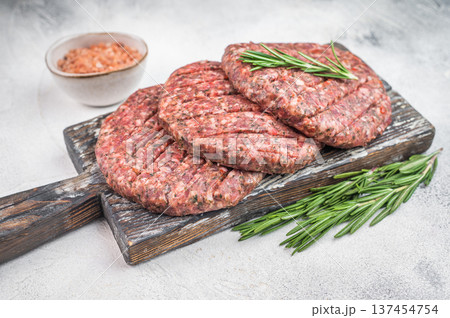 Raw mixed meat patties made from beef and lamb with herbs and salt. Light stone background flat lay with copy space for menu design. Raw mixed meat patties made from beef and lamb with herbs and salt. Light stone background flat lay with copy space for menu design. 137454754