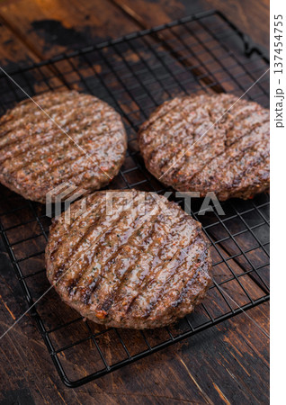 Grilled mixed beef and lamb cutlets with browned crust and savory surface. Top view of cooked meat burger patties on dark wood. 137454755