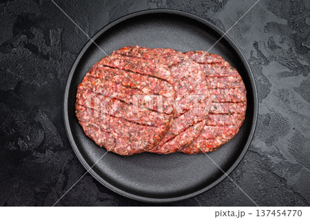 Fresh raw minced beef and lamb cutlets in plate with herbs. Flat lay on dark stone background for barbecue themes. Fresh raw minced beef and lamb cutlets in plate with herbs. Flat lay on dark stone background for barbecue themes. 137454770