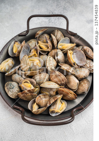 Steamed vongole mollusks in round pan on gray surface. Mediterranean shellfish composition with minimal style. Steamed vongole mollusks in round pan on gray surface. Mediterranean shellfish composition with minimal style. 137454839