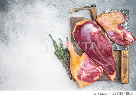 Raw duck meat cuts with breast and leg on wooden board with knife and thyme. Gamebird poultry game meat on gray background copy space. 137454868