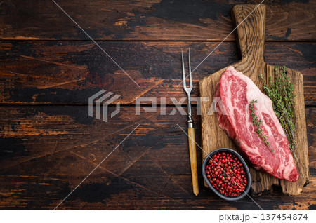 Raw beef chuck eye roll steak on wooden board with thyme and pepper. Marbled beef cut on dark wood background top view copy space.. Raw beef chuck eye roll steak on wooden board with thyme and pepper. Marbled beef cut on dark wood background top view copy space.. 137454874