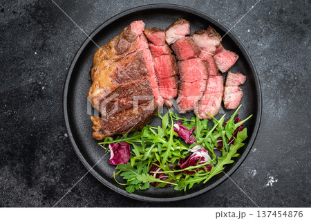 Pan fried beef chuckeye roll steak sliced and served with leafy greens. Gourmet beef dish with copy space top view. Pan fried beef chuckeye roll steak sliced and served with leafy greens. Gourmet beef dish with copy space top view. 137454876