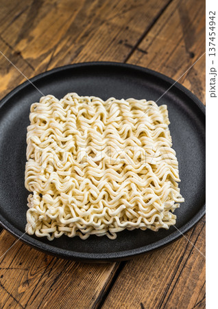 Raw wheat instant noodle brick with cilantro on black dish over vintage wood surface minimal Asian convenience food concept 137454942