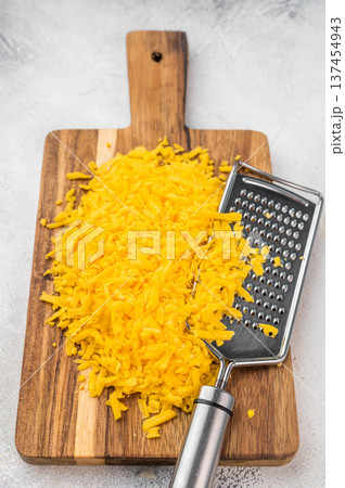 Cheddar cheese shreds and steel grater on wooden board over gray surface cooking ingredient texture for recipes and menus 137454943