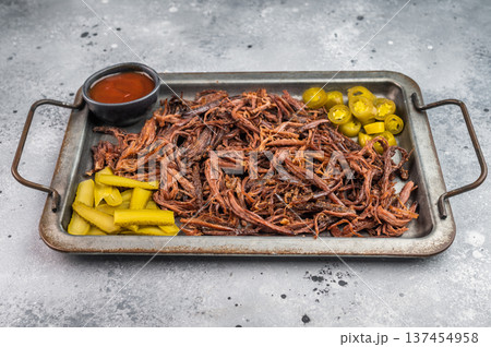 Pulled beef brisket with barbecue sauce, jalapeno and pickles on metal tray, top view with copy space on light background. 137454958