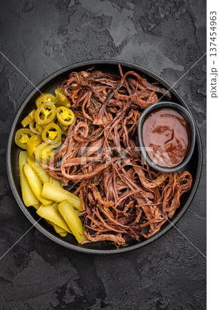 Smoked shredded brisket served with BBQ sauce and pickled vegetables, rustic American barbecue meal, overhead shot. 137454963