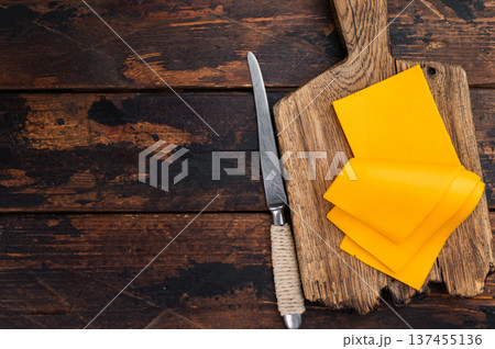 Sliced cheddar style cheese on wooden cutting board with knife over rustic table background and copy space for food design 137455136