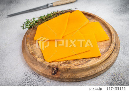 Cheddar cheese slices arranged on wooden plate with kitchen knife light concrete surface food background with copy space 137455153
