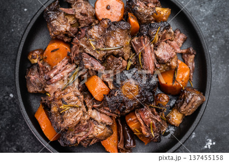Slow cooked oxtails with vegetables and herbs, hearty comfort food served on dark background, top view 137455158