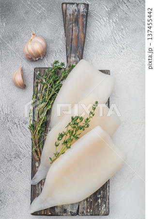 Fresh squid fillets with thyme and garlic on a rustic wooden board over a light textured background perfect for seafood and cooking themes. Fresh squid fillets with thyme and garlic on a rustic wooden board over a light textured background perfect for seafood and cooking themes. 137455442