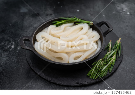 Raw calamari squid loops on black textured surface with herbs offering minimal ocean seafood ingredient concept for culinary design 137455462