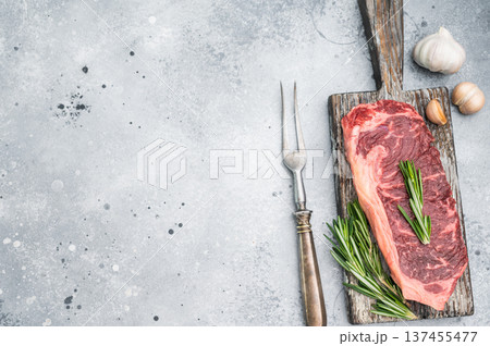 Premium New York steak raw and marbled with rosemary placed on rustic board on bright stone background great for gourmet cooking concepts Premium New York steak raw and marbled with rosemary placed on rustic board on bright stone background great for gourmet cooking concepts 137455477