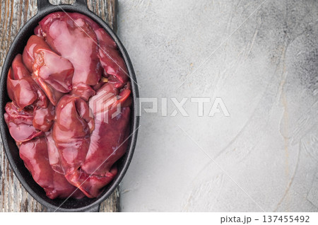 Raw chicken liver in a black pan on a wooden board, garnished with rosemary, set against a grey background. Raw chicken liver in a black pan on a wooden board, garnished with rosemary, set against a grey background. 137455492