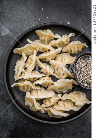 Tasty steamed gyoza wontons arranged on a black plate over concrete background. Authentic asian appetizer for menus and culinary projects. Tasty steamed gyoza wontons arranged on a black plate over concrete background. Authentic asian appetizer for menus and culinary projects. 137455521