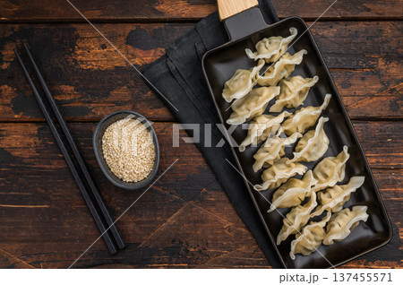 Traditional gyoza, jiaozi or mandu served as an authentic oriental appetizer. Steamed Asian dumplings arranged on a dark rectangular plate with chopsticks on a rustic wooden table. 137455571