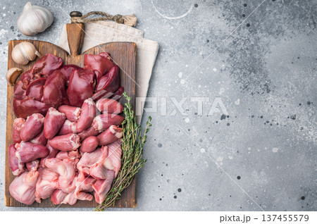 Uncooked chicken liver, hearts, gizzards arranged on weathered board. Speckled grey surface creates modern food photo vibe. 137455579