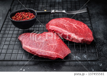 Raw Wagyu top blade steaks with rich marbling on metal grate next to red pepper and vintage fork over dark stone surface perfect for gourmet stock images. 137455581