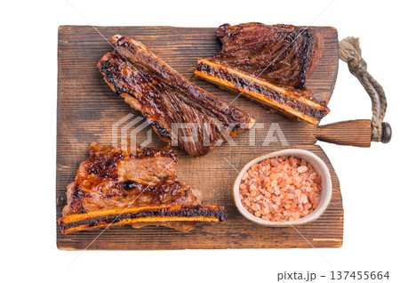 Gourmet grilled beef short ribs served on a rustic wooden board with a bowl of pink Himalayan salt. Clean white background. 137455664
