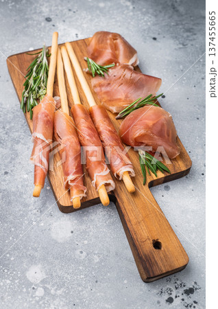 Gourmet Italian Antipasto with prosciutto crudo, grissini breadsticks, and olives on a rustic wooden board. Top view with copy space. 137455665