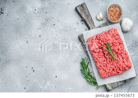 Fresh raw ground mince beef meat with rosemary on parchment over rustic wooden board and concrete background ideal for cooking and protein visuals. 137455673
