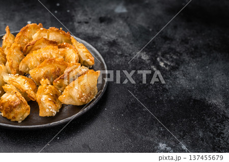 Crunchy gyoza wonton dumplings on dark stone background savory Asian dish with golden crust and sesame garnish 137455679
