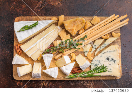 Brie Camembert Parmesan and Roquefort arranged with nuts herbs and breadsticks on a rustic wooden board over a dark textured background. Brie Camembert Parmesan and Roquefort arranged with nuts herbs and breadsticks on a rustic wooden board over a dark textured background. 137455689