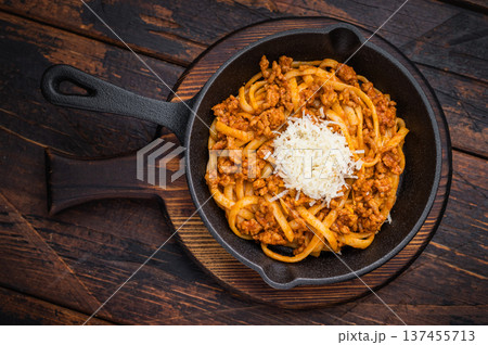 Classic pasta bolognese with savory meat ragu and parmesan shreds served in rustic skillet on vintage wooden surface with herbs. Classic pasta bolognese with savory meat ragu and parmesan shreds served in rustic skillet on vintage wooden surface with herbs. 137455713