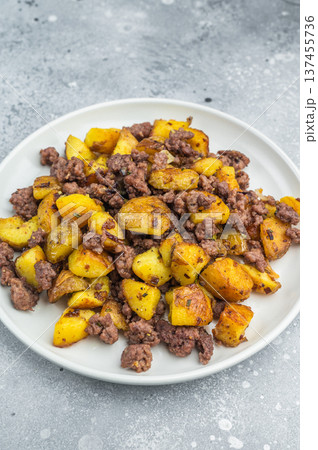 Crispy fried potatoes with ground beef served on a white plate, hearty homemade hash on a rustic grey background.. 137455736